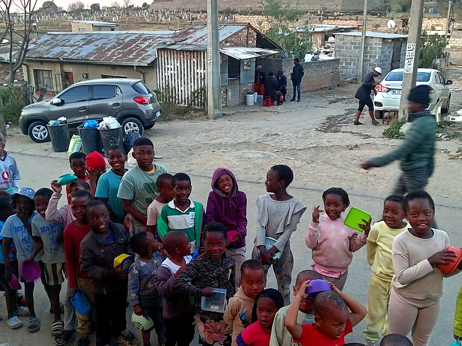 A long line of smiling children holding containers at a community feeding scheme
