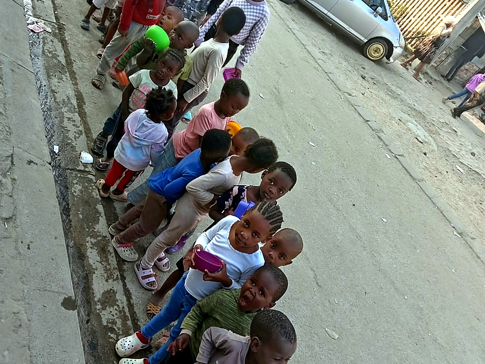 Children queuing with bowls along a township street during a community feeding scheme